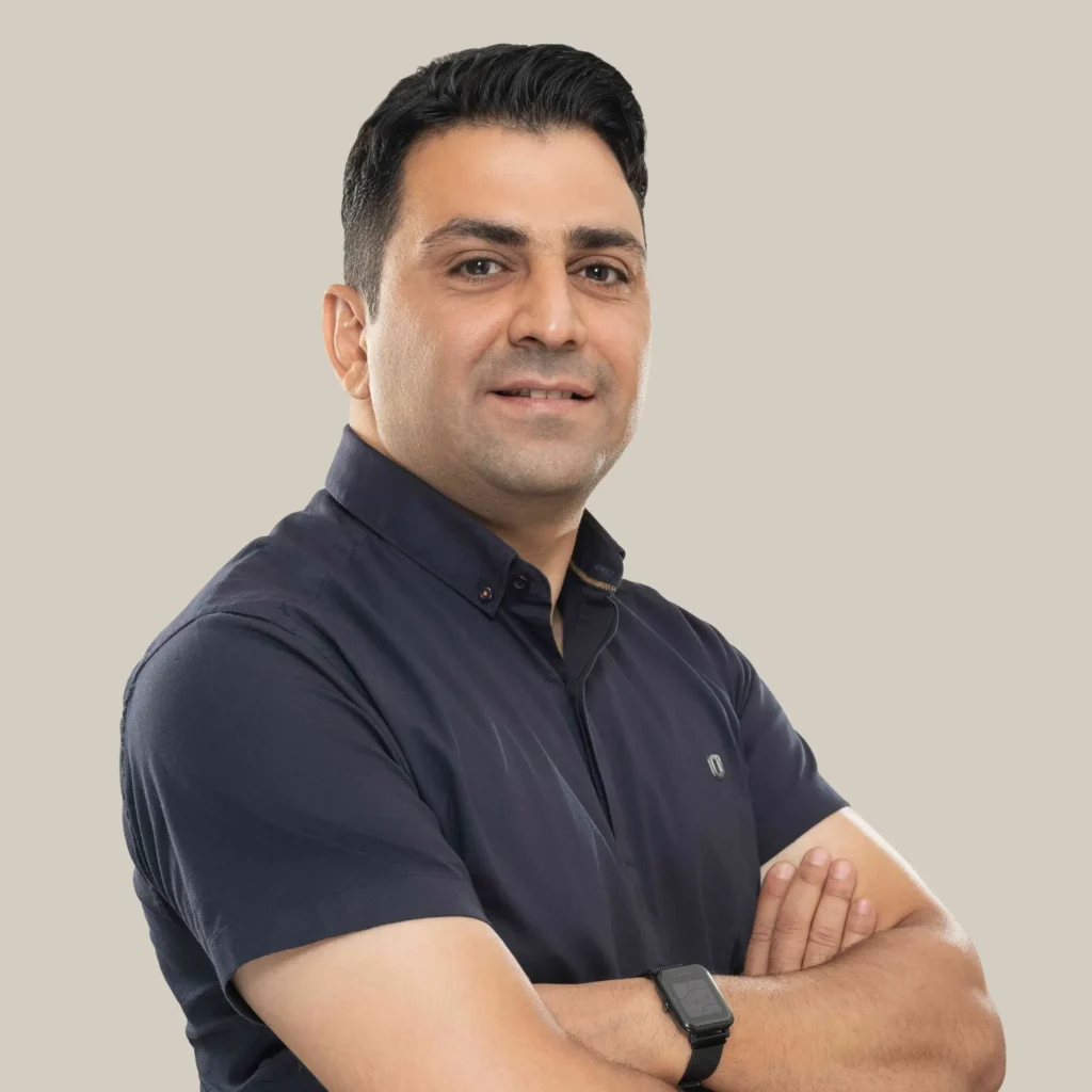 تصویر دانیال قالیباف مدیر دفتر تهران وی دیجی که با بلوز سورمه ای آستین کوتاه دست به سینه و کمی متمایل به سمت راست ما ایستاده و داره لبخند میزنه